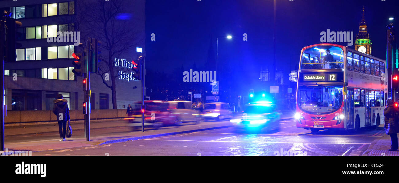 Met police car with blue flashing lights illuminating night sky on Westminster Bridge with red London bus waiting at traffic light England UK Stock Photo