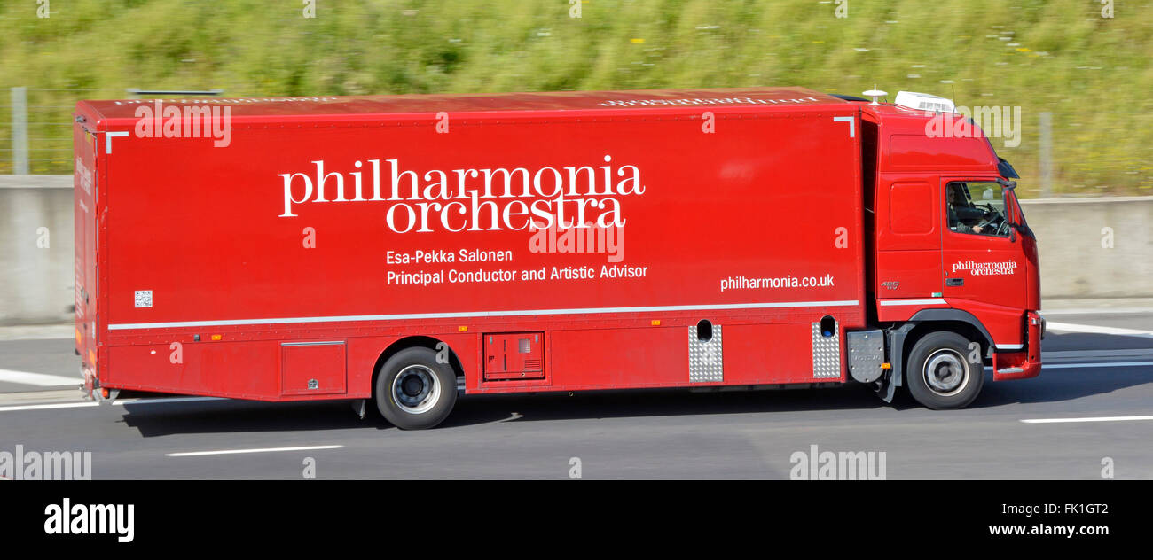 Truck driver in cab of Philharmonia Orchestra side view of red lorry driving along M25 motorway Essex England UK Stock Photo