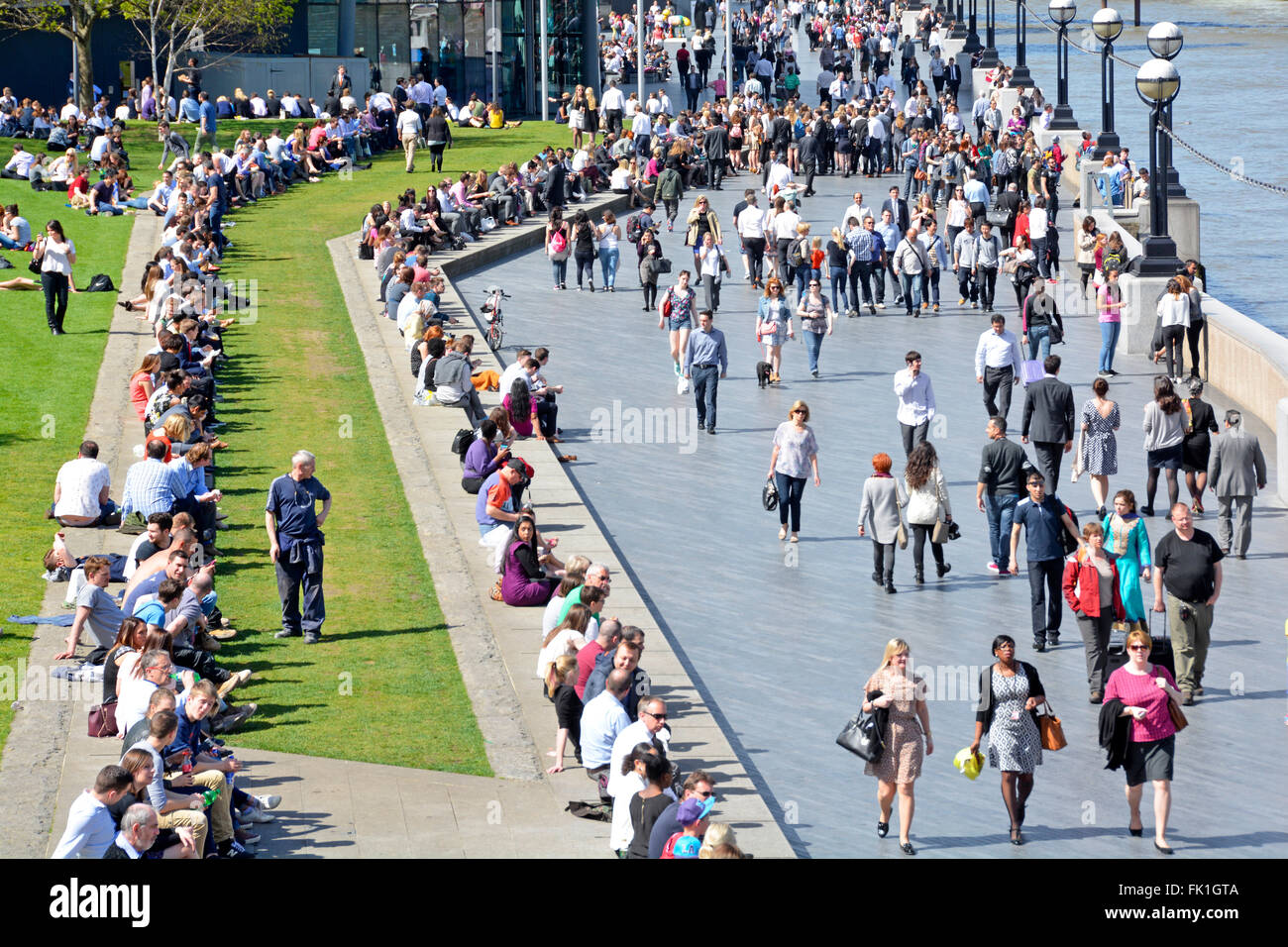 Spring sunshine for tourists & office workers to enjoy along the South Bank beside River Thames at City Hall Southwark in more London England UK Stock Photo