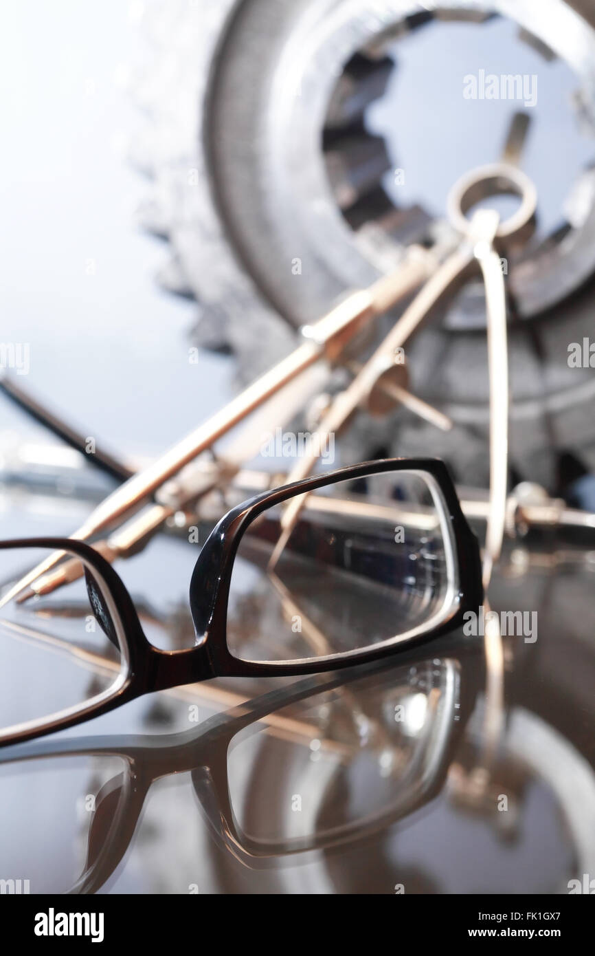 Industrial concept. Spectacles near divider and gear on glass surface ...