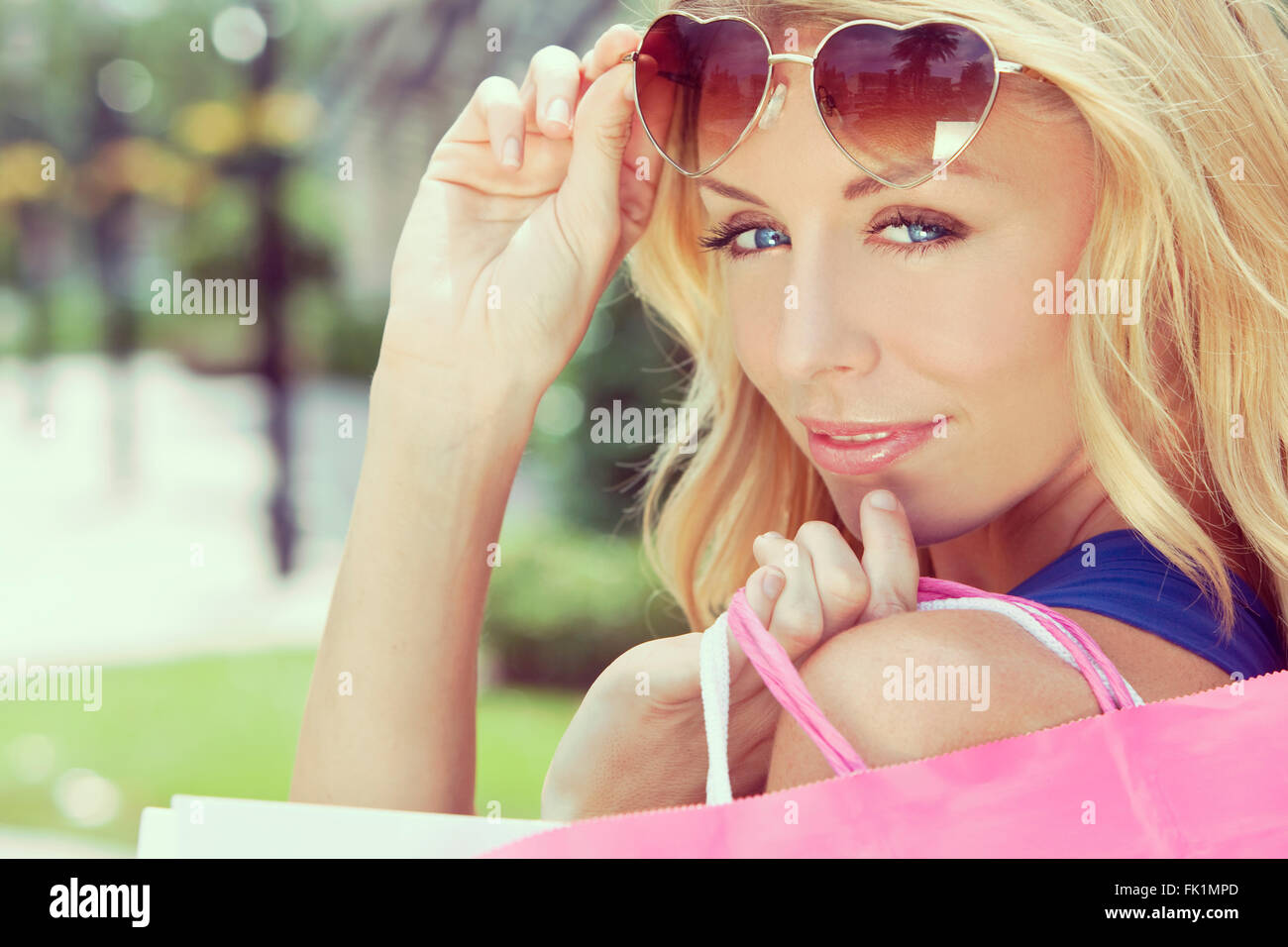 Instagram style happy and fashionable woman with colorful pink and white shopping bags and wearing heart shaped sunglasses Stock Photo