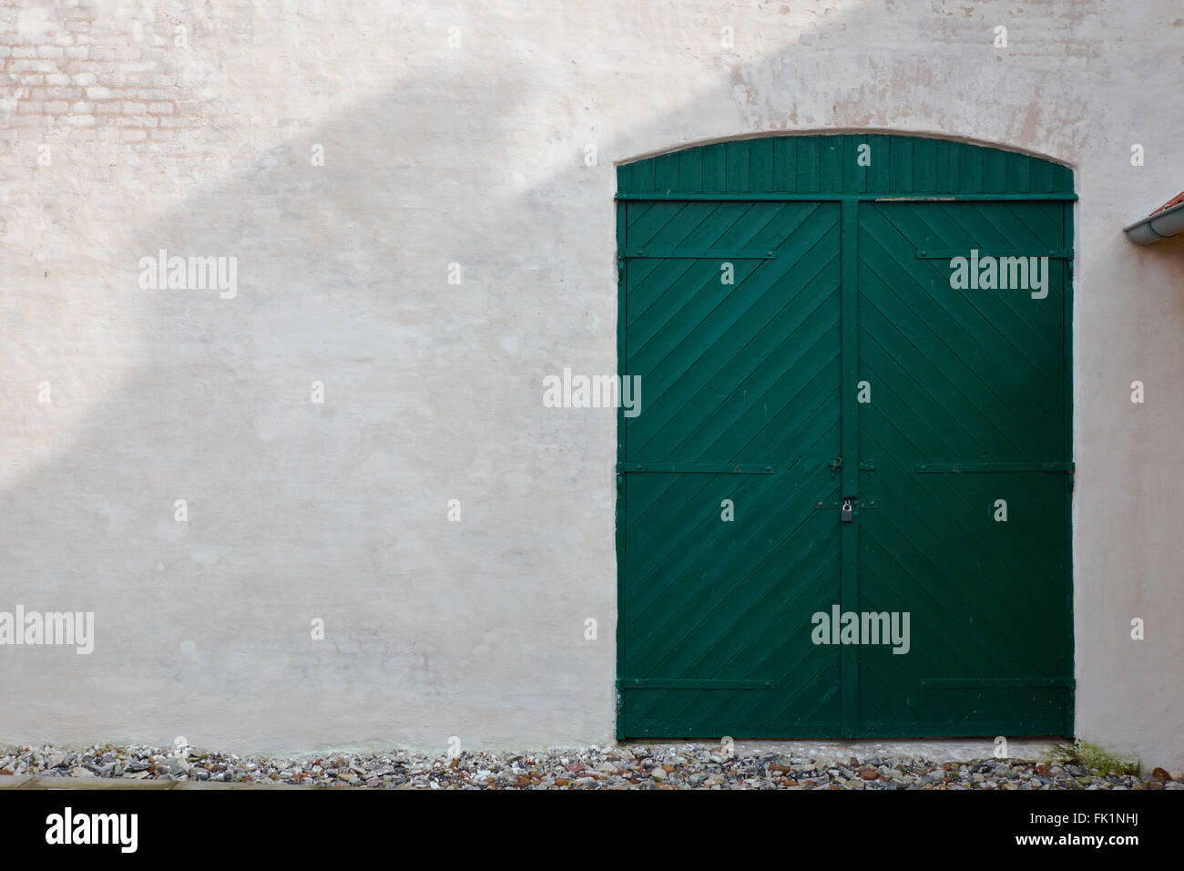 Old green wood barn door type in a light colored plastered facade of bricks Stock Photo