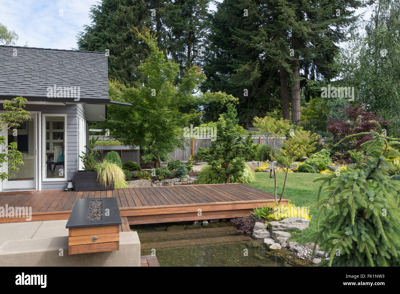 Back yard of a contemporary Pacific Northwest home featuring a deck spanning a creek-like water feature with a landscaped lawn i Stock Photo