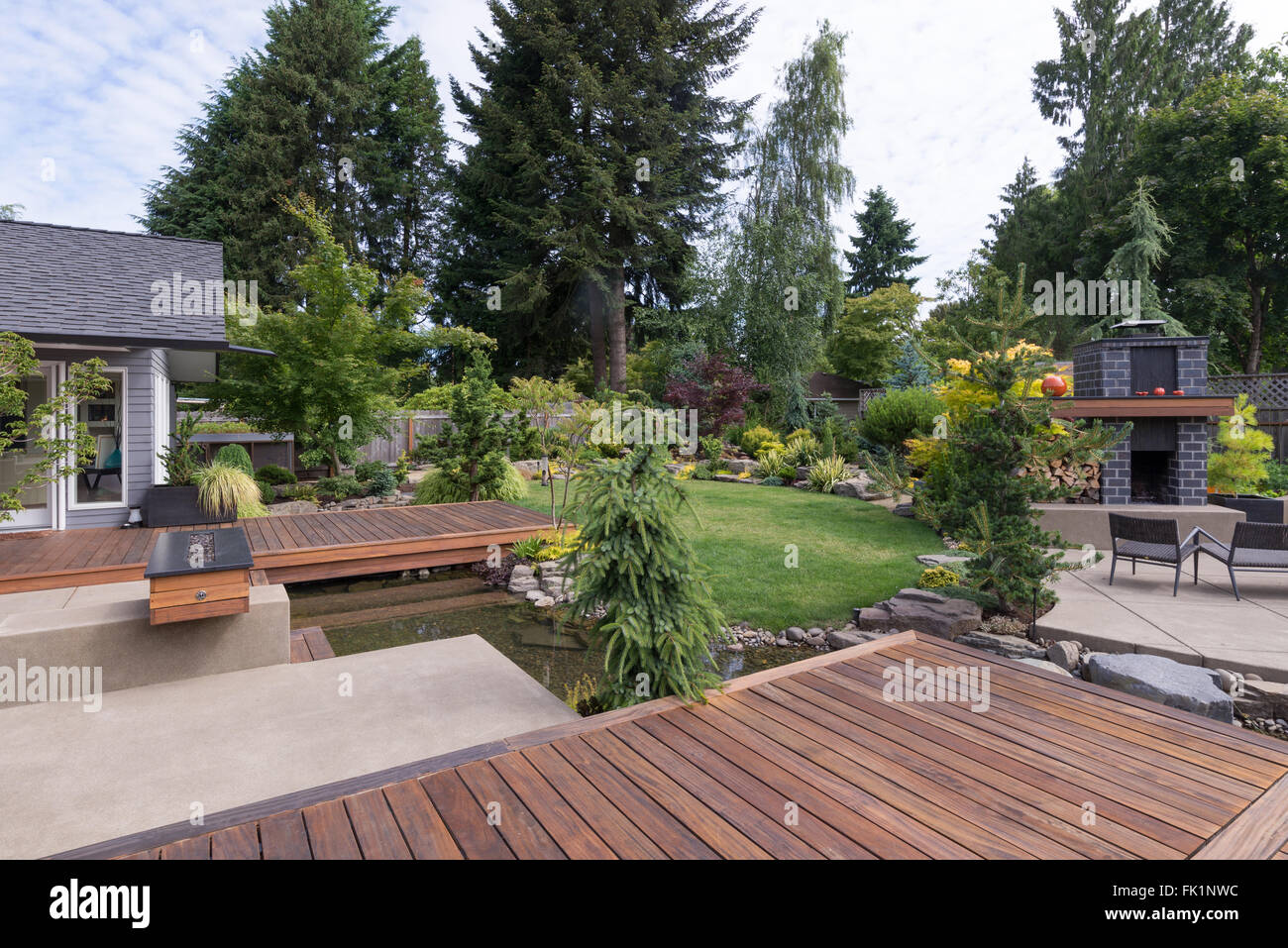 Back yard of a contemporary Pacific Northwest home featuring a deck a spanning creek-like water feature with a landscaped lawn a Stock Photo