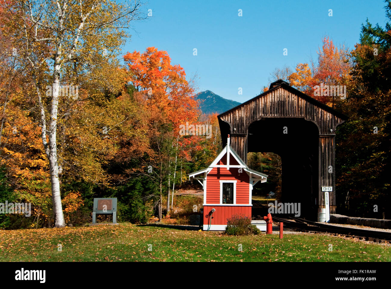 Clark's covered bridge lies on a railroad track crossing a river on an autumn day with vibrant foliage in the White Mountains of New Hampshire. Stock Photo