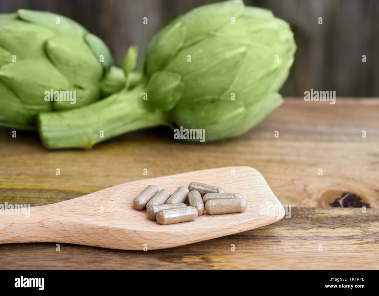 Selective focus on Artichoke supplements on wooden spoon, with out of focus Artichoke in the background, on wooden table Stock Photo