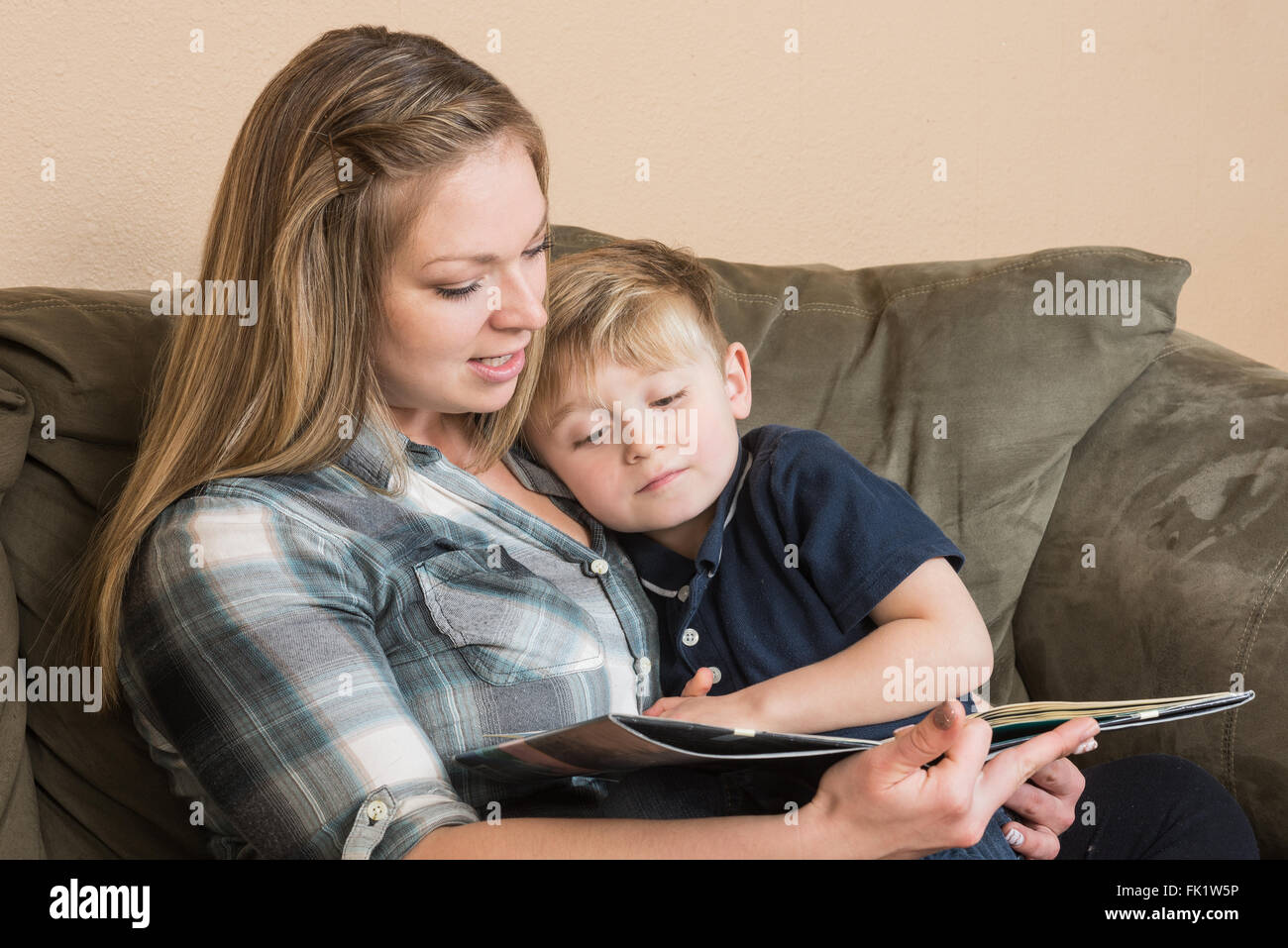 A young boy snuggles into his mother as she reads him a book. Stock Photo