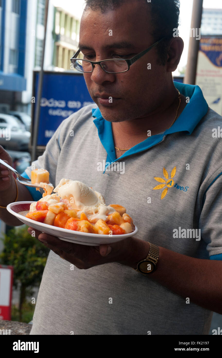 Sri Lankan office worker enjoying fresh fruit salad with ice cream, at a store in the Fort district, Colombo Stock Photo