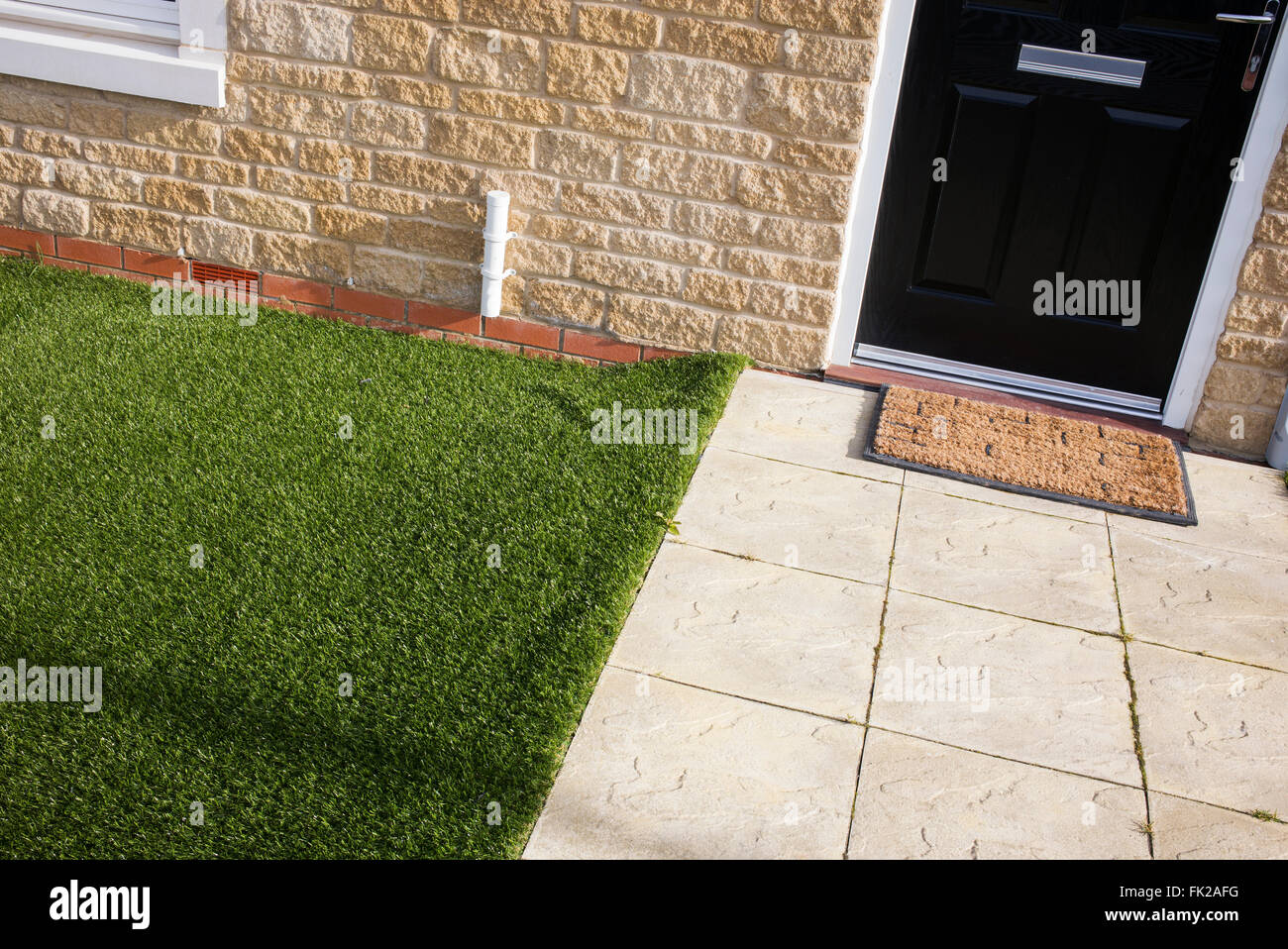 Artificial grass / astro turf meets paving slabs on a new build housing estate. Bicester, Oxfordshire, England Stock Photo