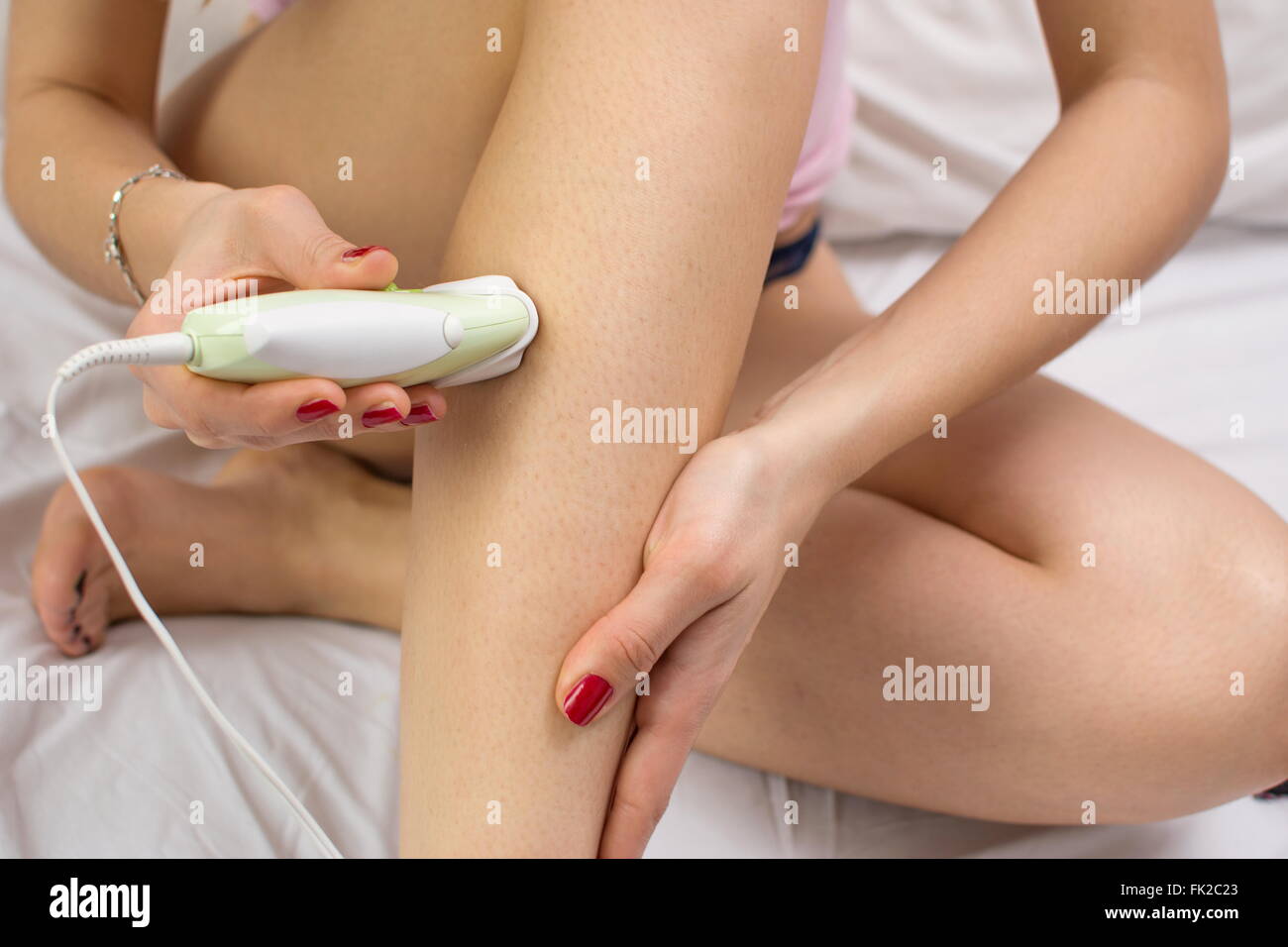 Girl epilates her leg with an epilator on the bed Stock Photo