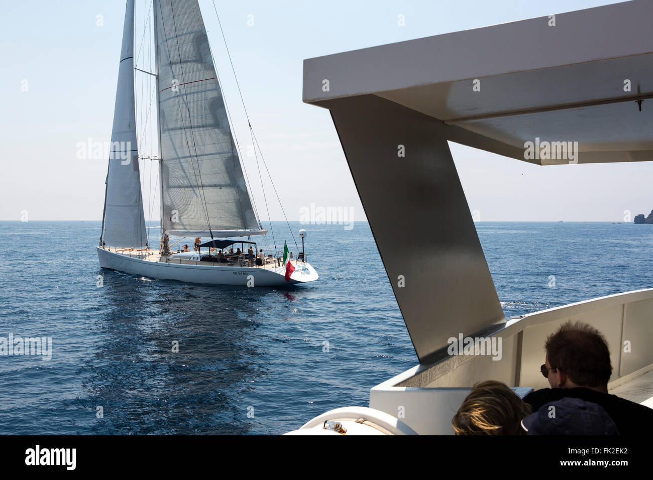 Passengers relaxing on a boat trip in Italy as a large yacht with sail