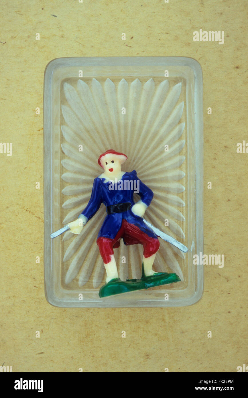 Plastic model of pirate or soldier or highwayman holding two swords lying in small glass tray with sunburst effect Stock Photo
