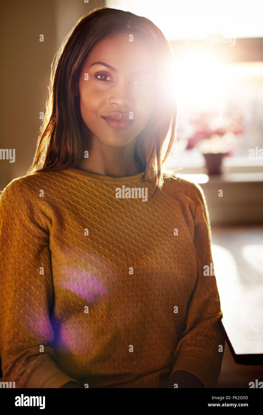 Smiling attractive young black woman relaxing at home sitting at a ...