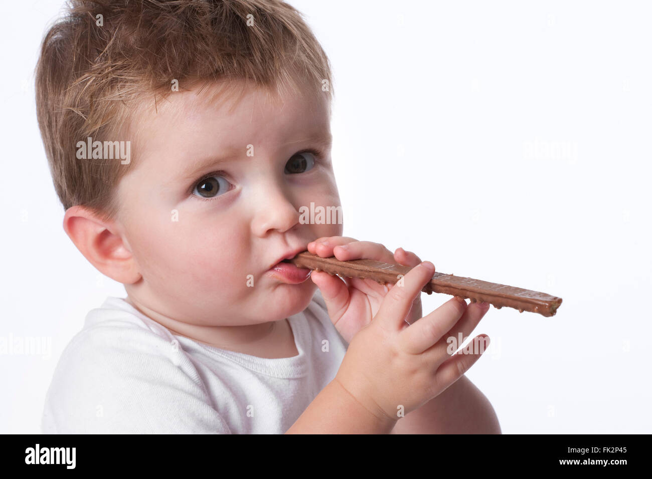 Toddler boy is eating a chocolate snack on white background Stock Photo
