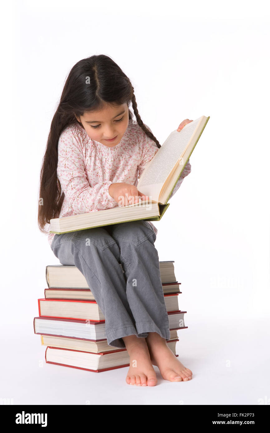 Little Girl Is Reading A Large Book sitting on a pile of books on white background Stock Photo