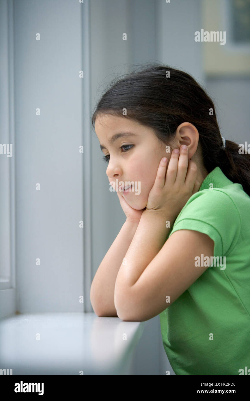 Little girl is looking out of the window with a sad face Stock Photo