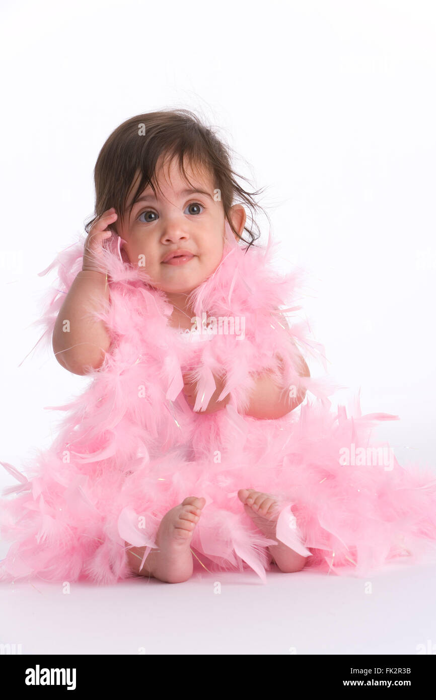 Baby Girl Sitting On The Floor Dressed In Pink Feathers Like A Diva on white background Stock Photo