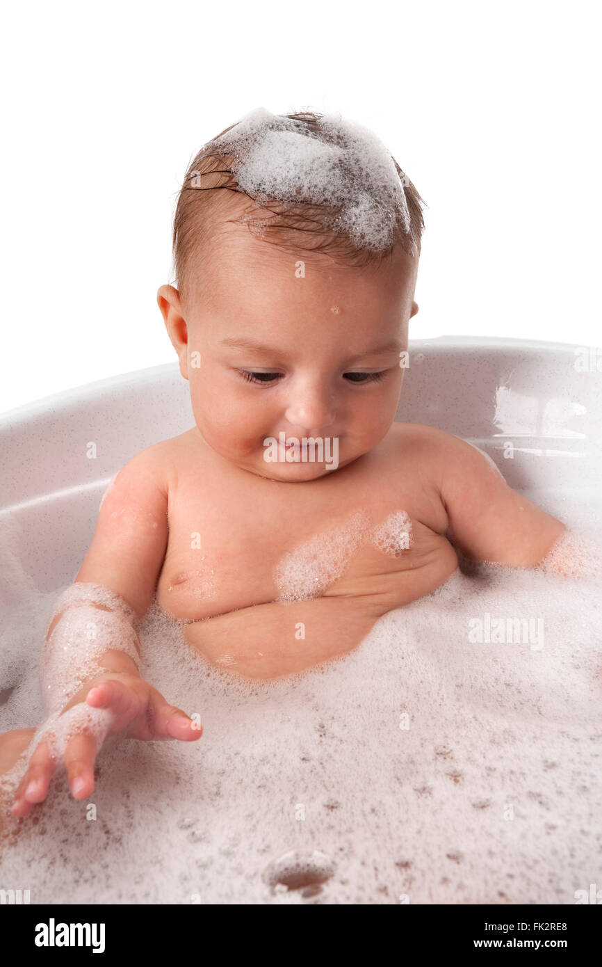 Baby girl is looking at bubbles in bathtub with foam on her head on white background Stock Photo
