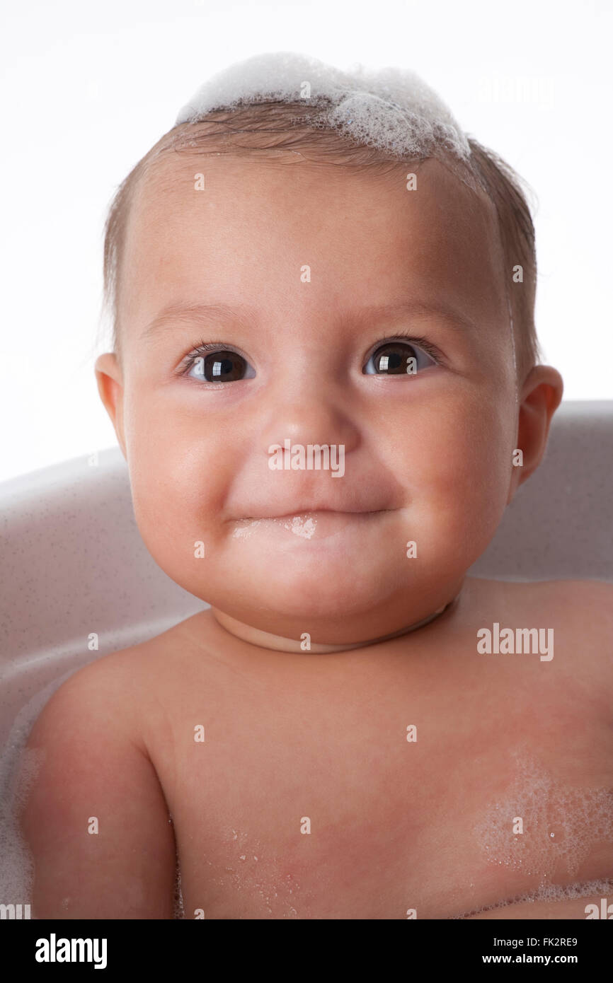 Baby Girl Sitting In Bathtub With Soap On Her Head on white background Stock Photo