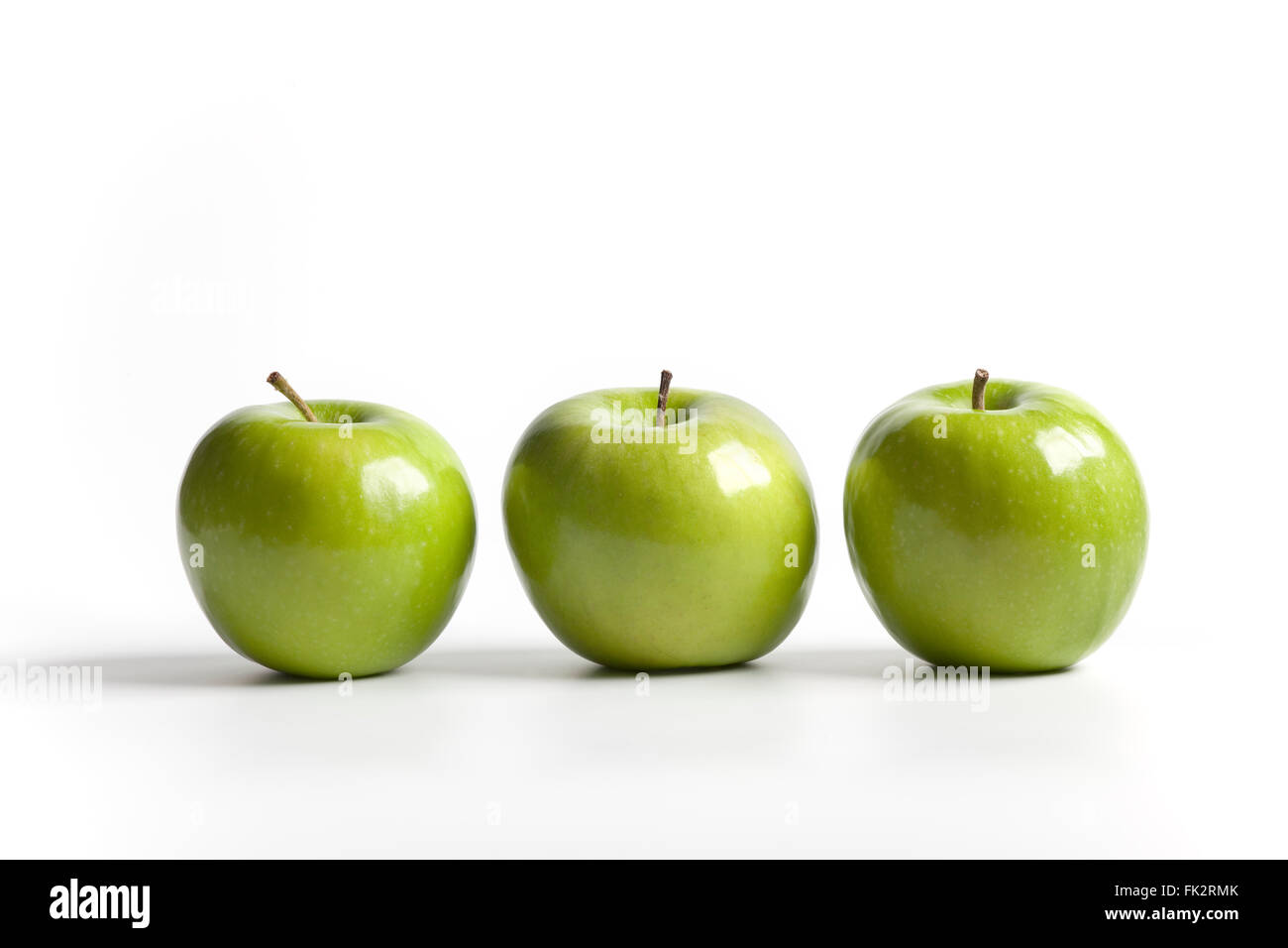 Three green shiny Granny Smith apples on a row on white background Stock Photo