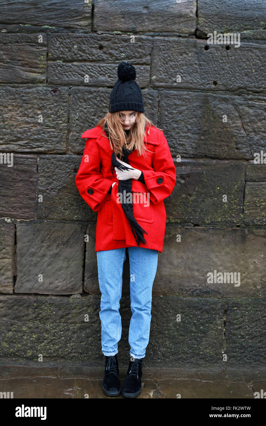 Woman in red jacket leaning against a stone wall in the rain and sleet ...