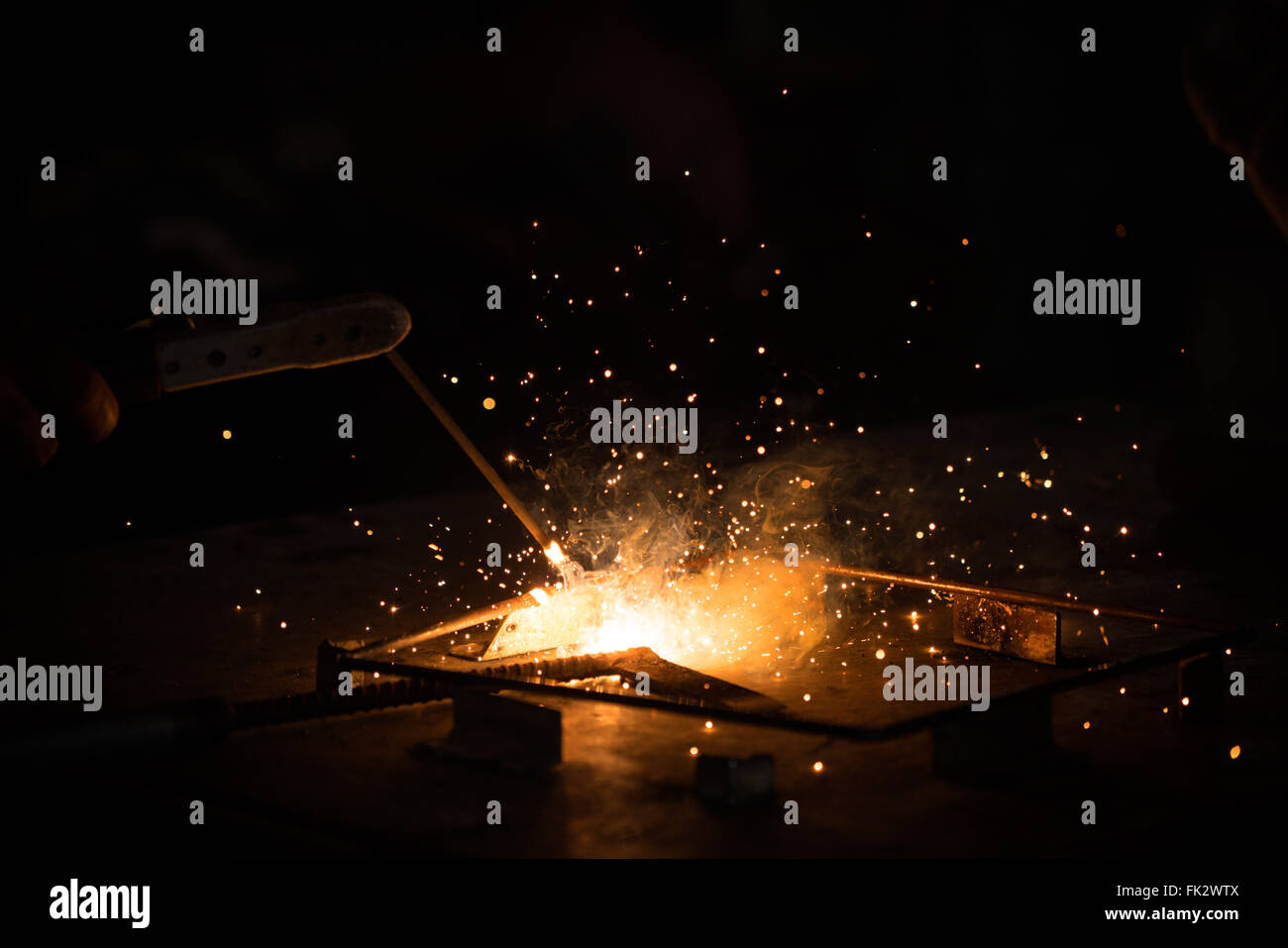 Welding, metal working on dark background, with golden bokeh and flare of sparks. Technician workshop, manufacturing industry, or construction worker Stock Photo