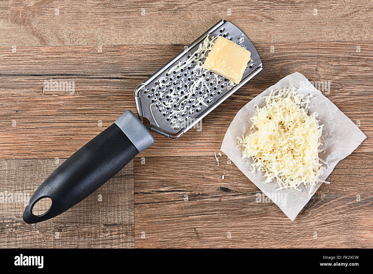 Parmesan Cheese and grater on a wood kitchen table. Some grated cheese is on a piece of parchment paper next to the grater. High Stock Photo