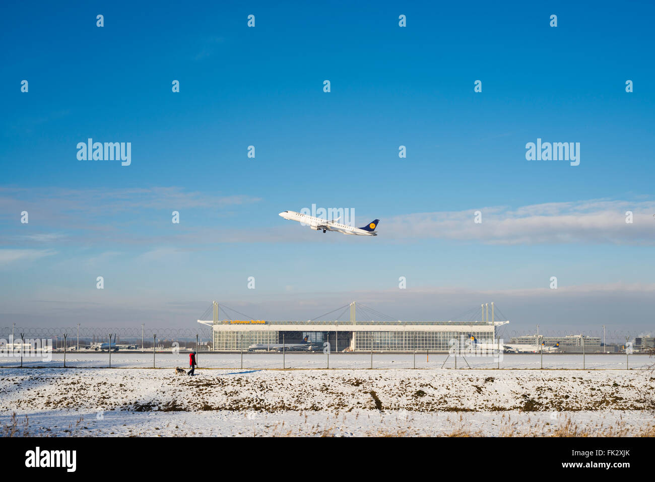 Stroller with dog along security fence in front of an airplane taking off from south runway at Munich Airport on a winter day Stock Photo