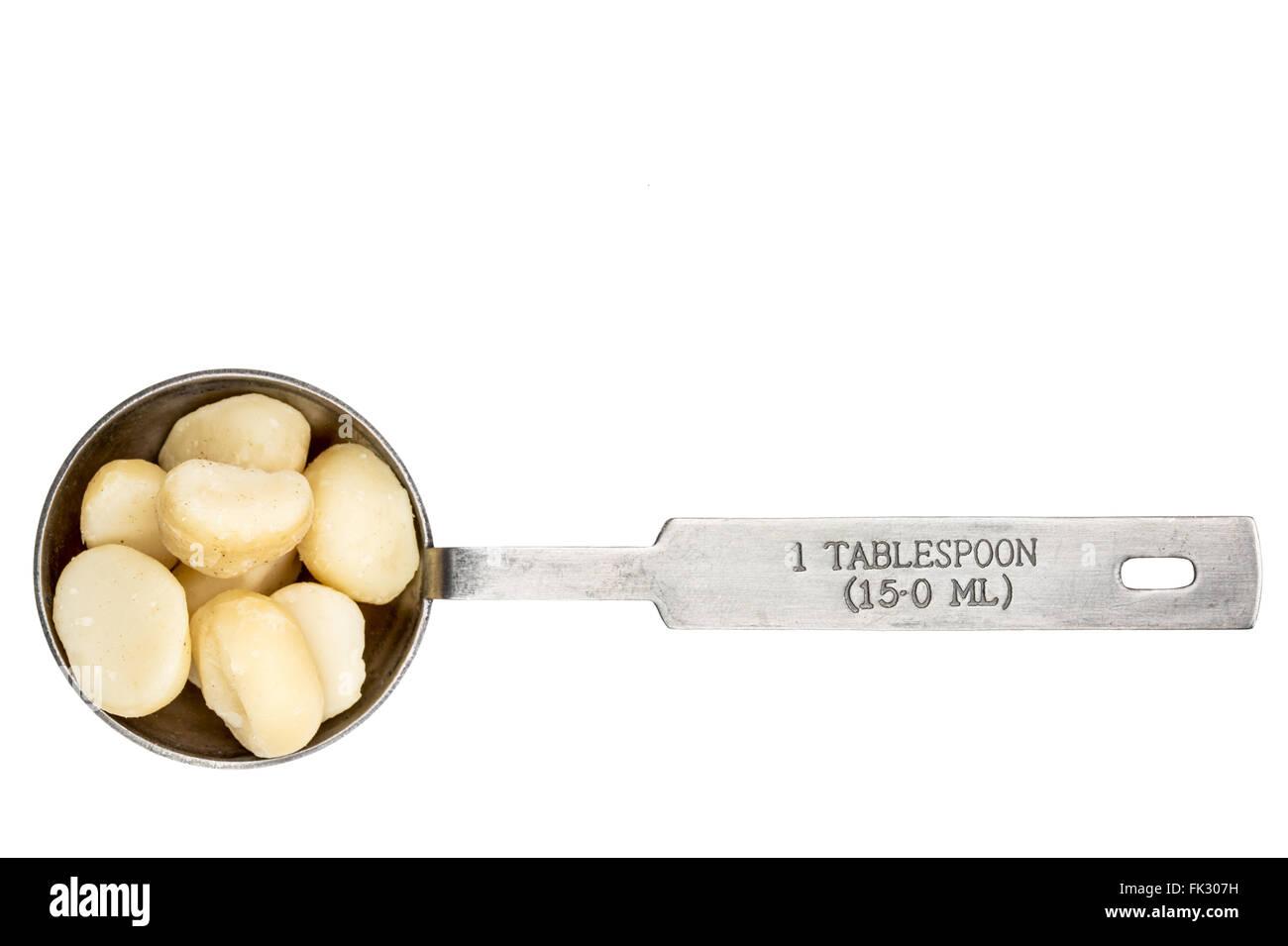 macadamia nuts in a metal measuring tablespoon isolated on white Stock Photo