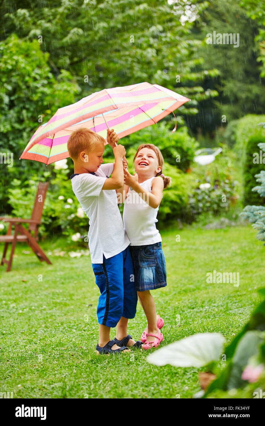 Two children standing under an umbrella in rain in a garden Stock Photo