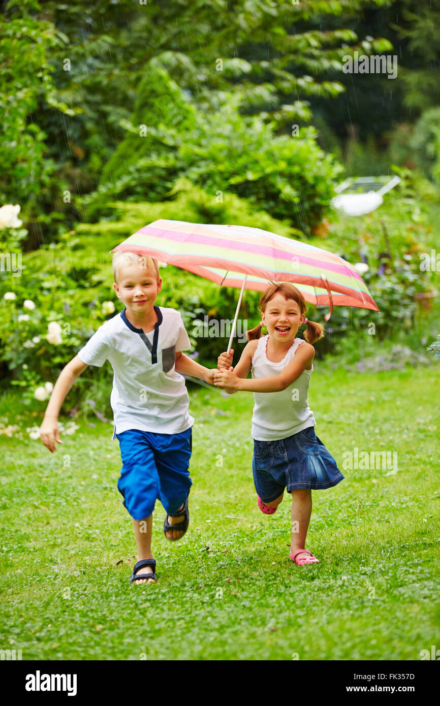 Two happy children running under an umbrella in the rain in a garden Stock Photo