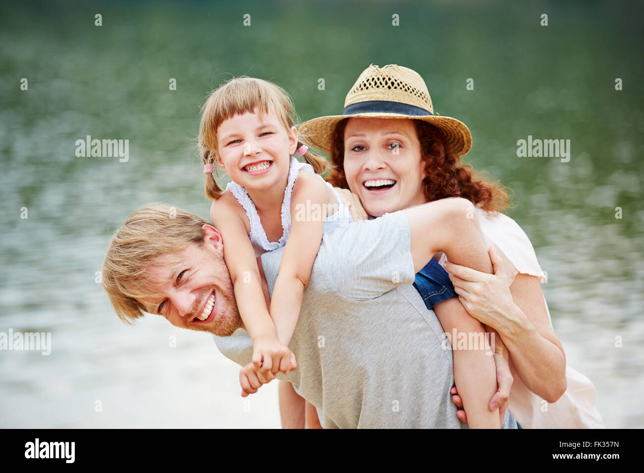 Happy family at water in summer carrying daughter for piggyback ride Stock Photo