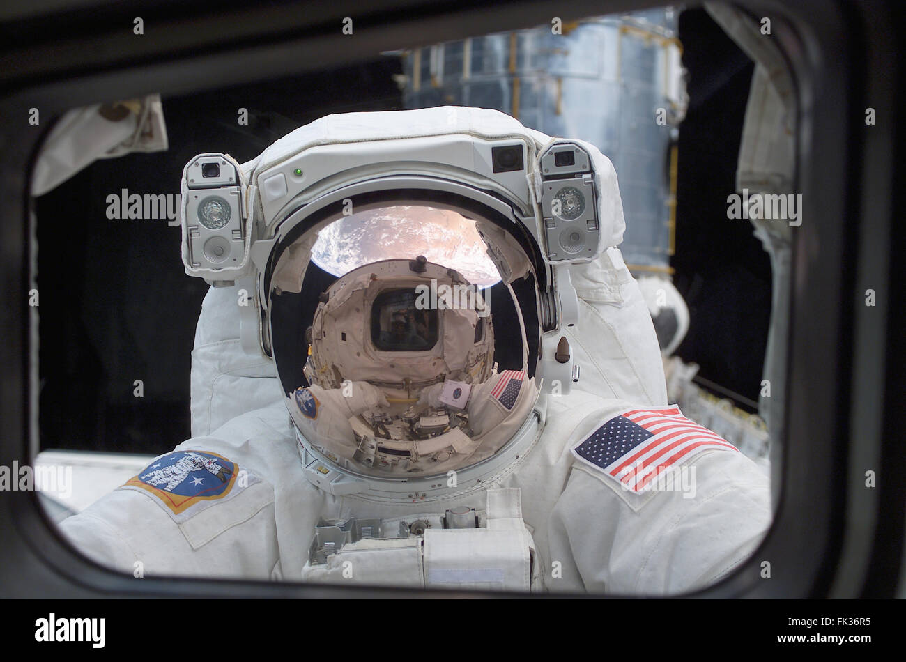 NASA astronaut John Grunsfeld peers into the crew cabin of the Space Shuttle Columbia from outer space during the first STS-109 extravehicular activity March 4, 2002 in Earth Orbit. Grunsfeld's helmet visor, with the sunshield now in place, displays mirrored images of the Earth and the Space Shuttle Columbia's aft cabin. Stock Photo
