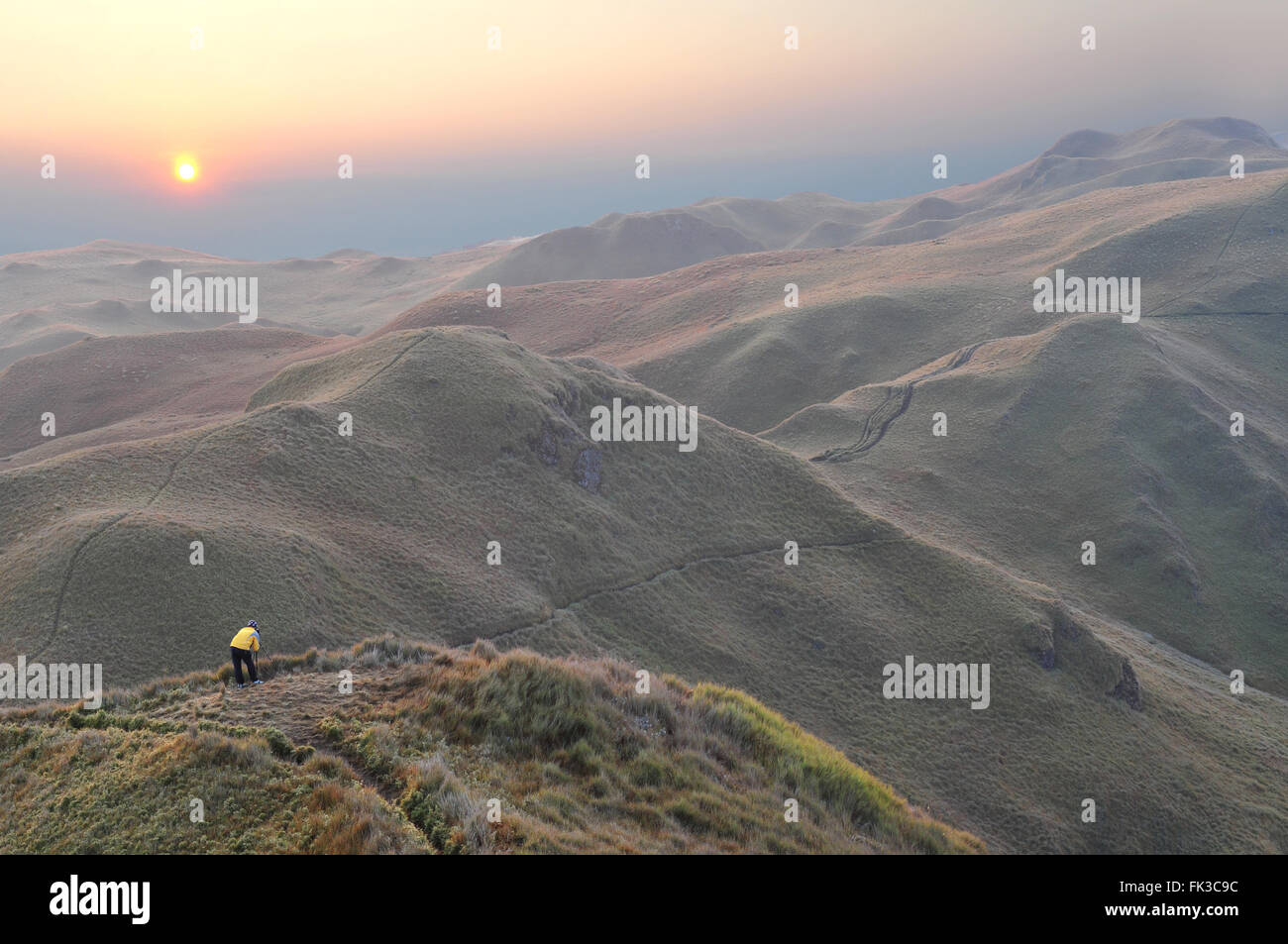 A lone photographer on top of a hill on peaceful mountain ranges. Stock Photo