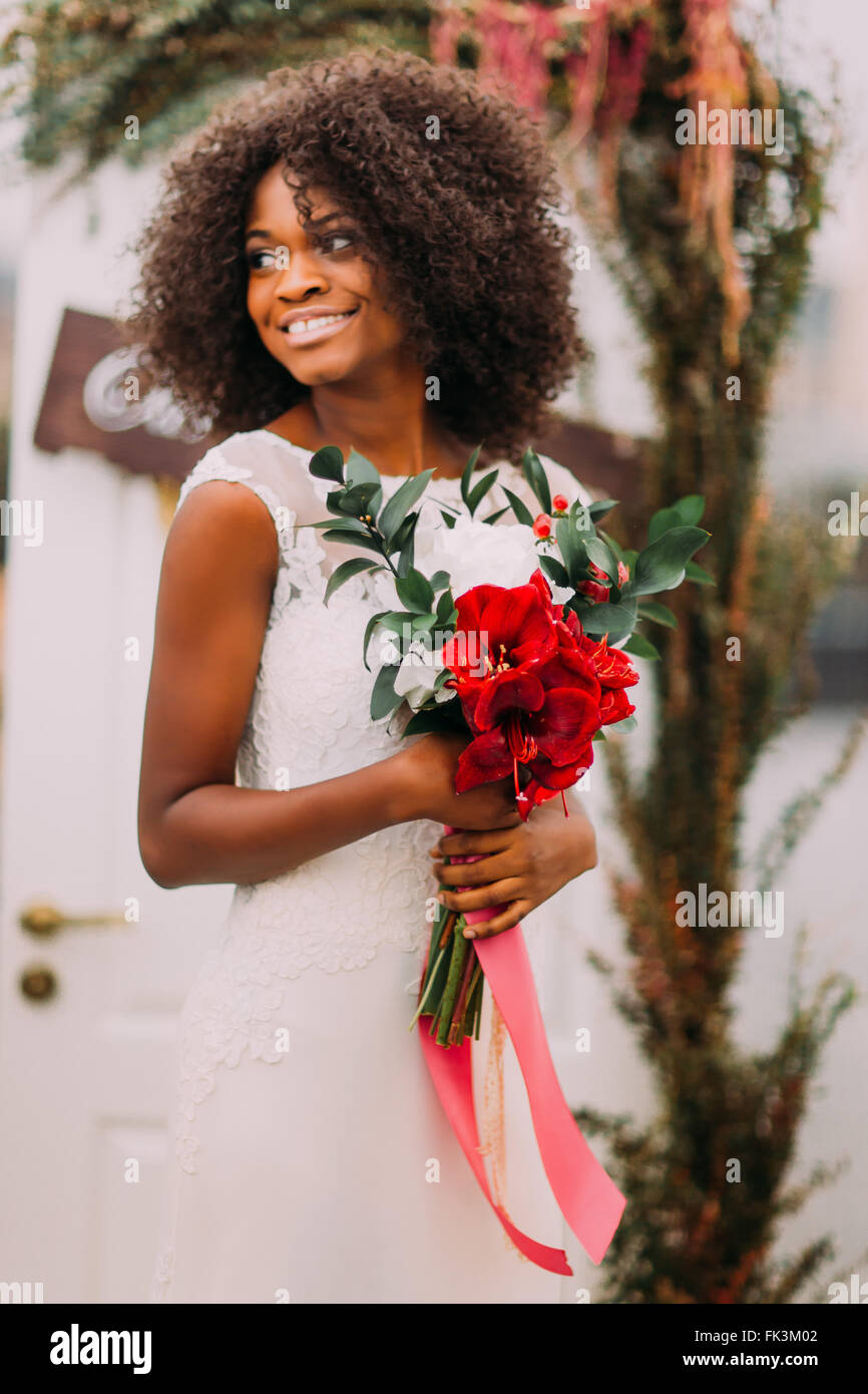 Beautiful african moony bride smiling with bouquet of red flowers on the wedding ceremony Stock Photo