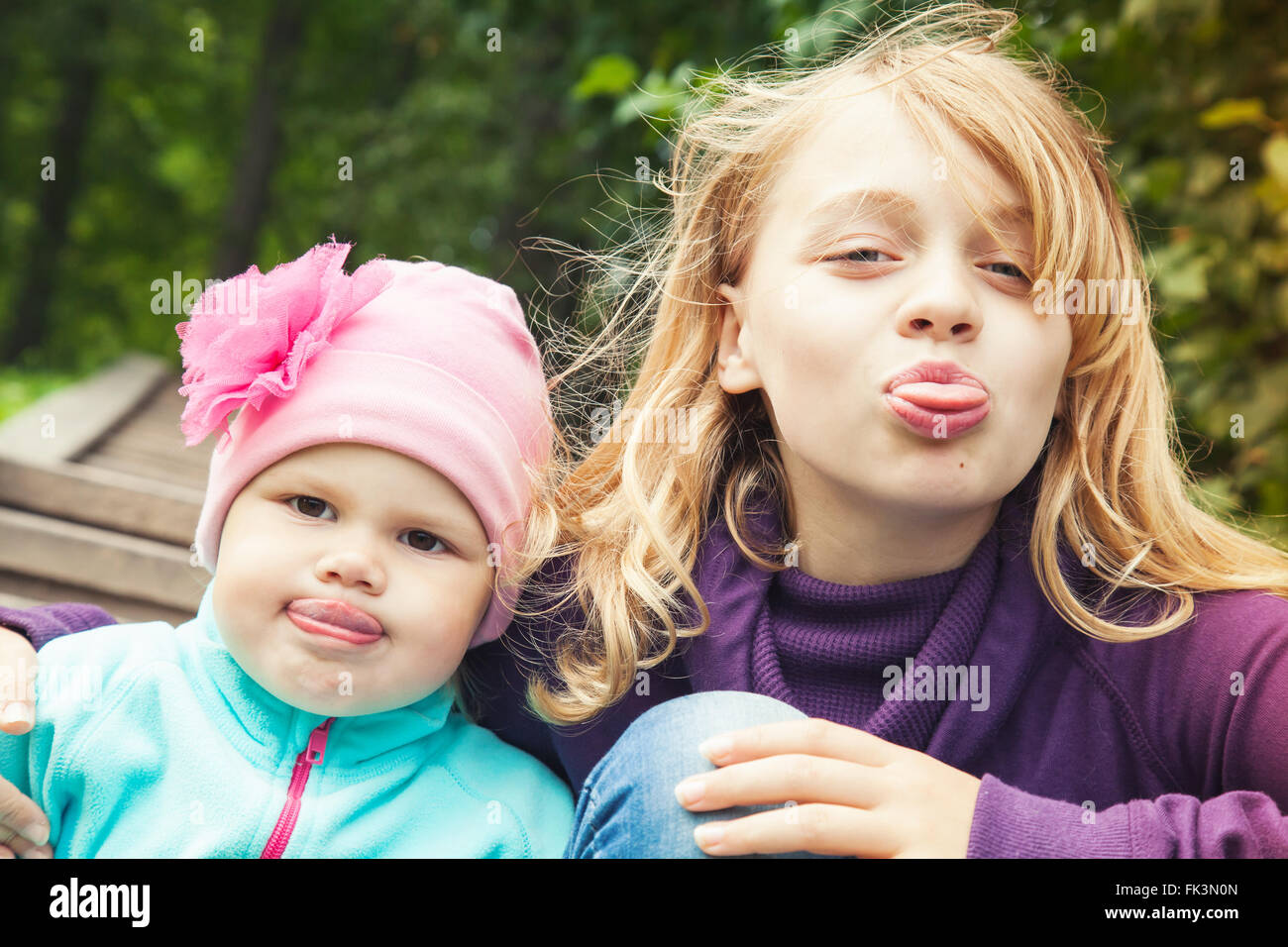 Funny little blond Caucasian sisters show tongues. Close up outdoor portrait with tonal correction photo filter effect Stock Photo