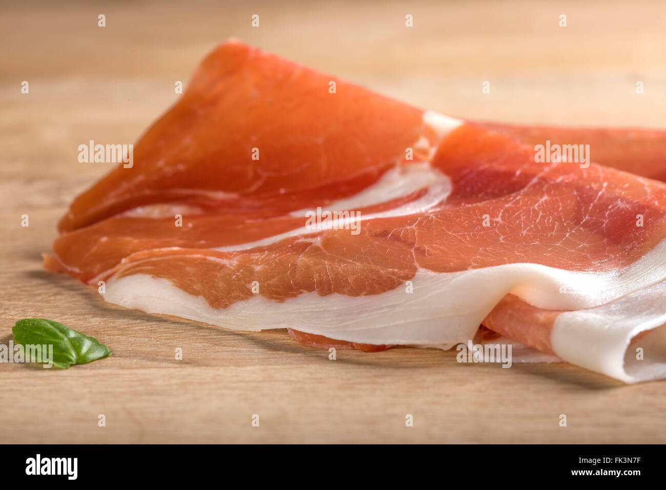 Thin slices of prosciutto on wooden cutting board Stock Photo