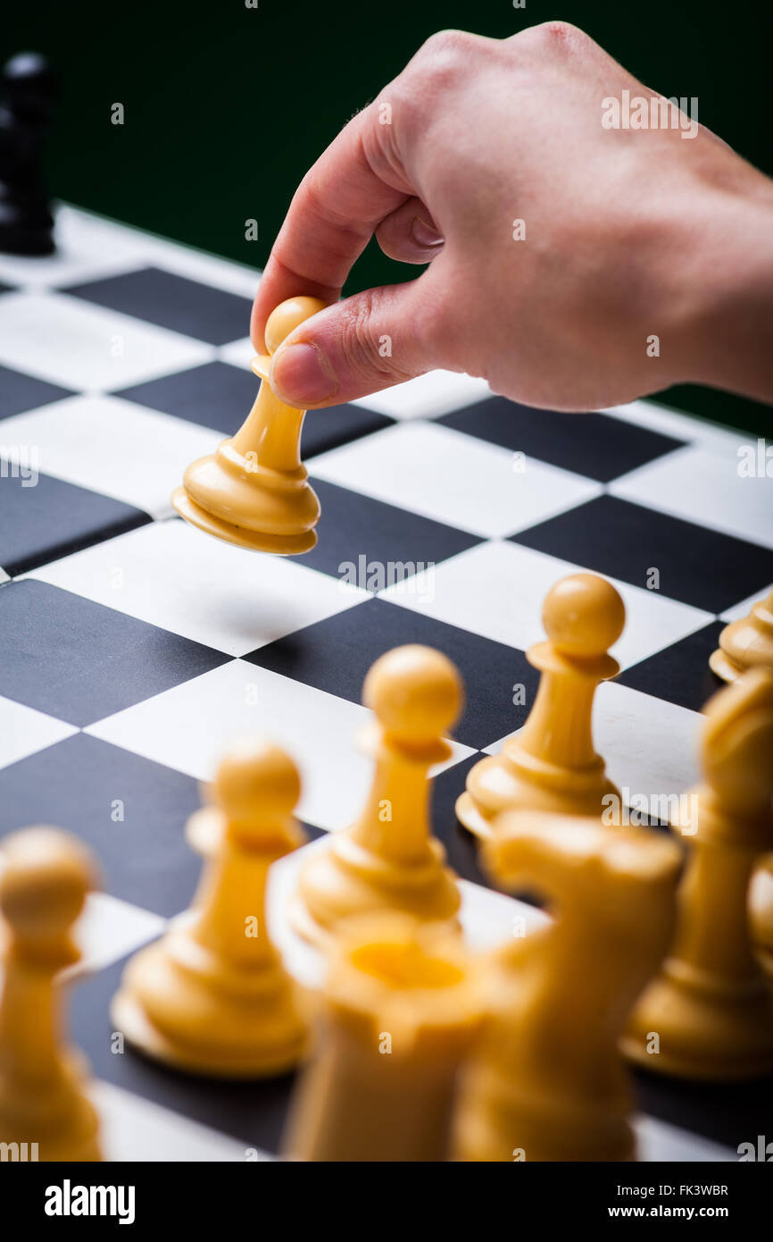Close-up image of a chess board with chess pieces and a human hand ...
