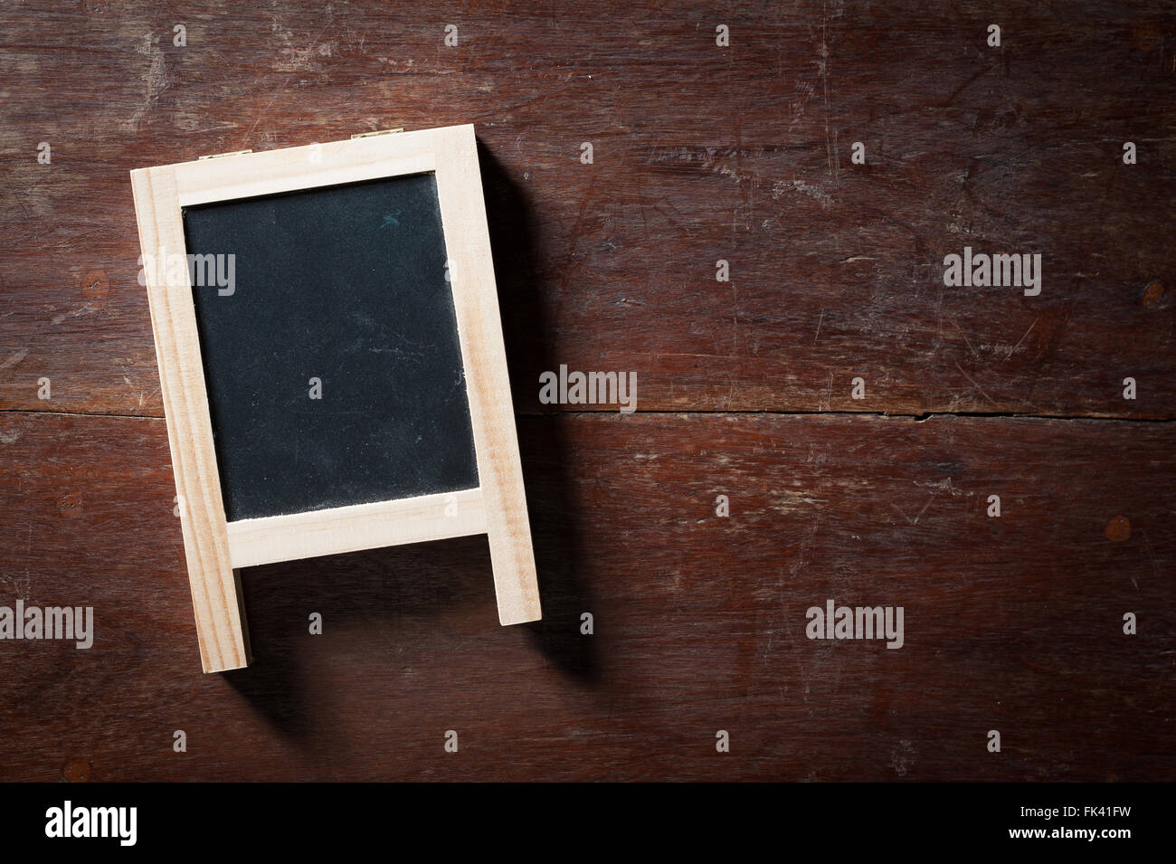 Small A-frame black board with blank area for text or message on rustic wood table with low key scene. Stock Photo