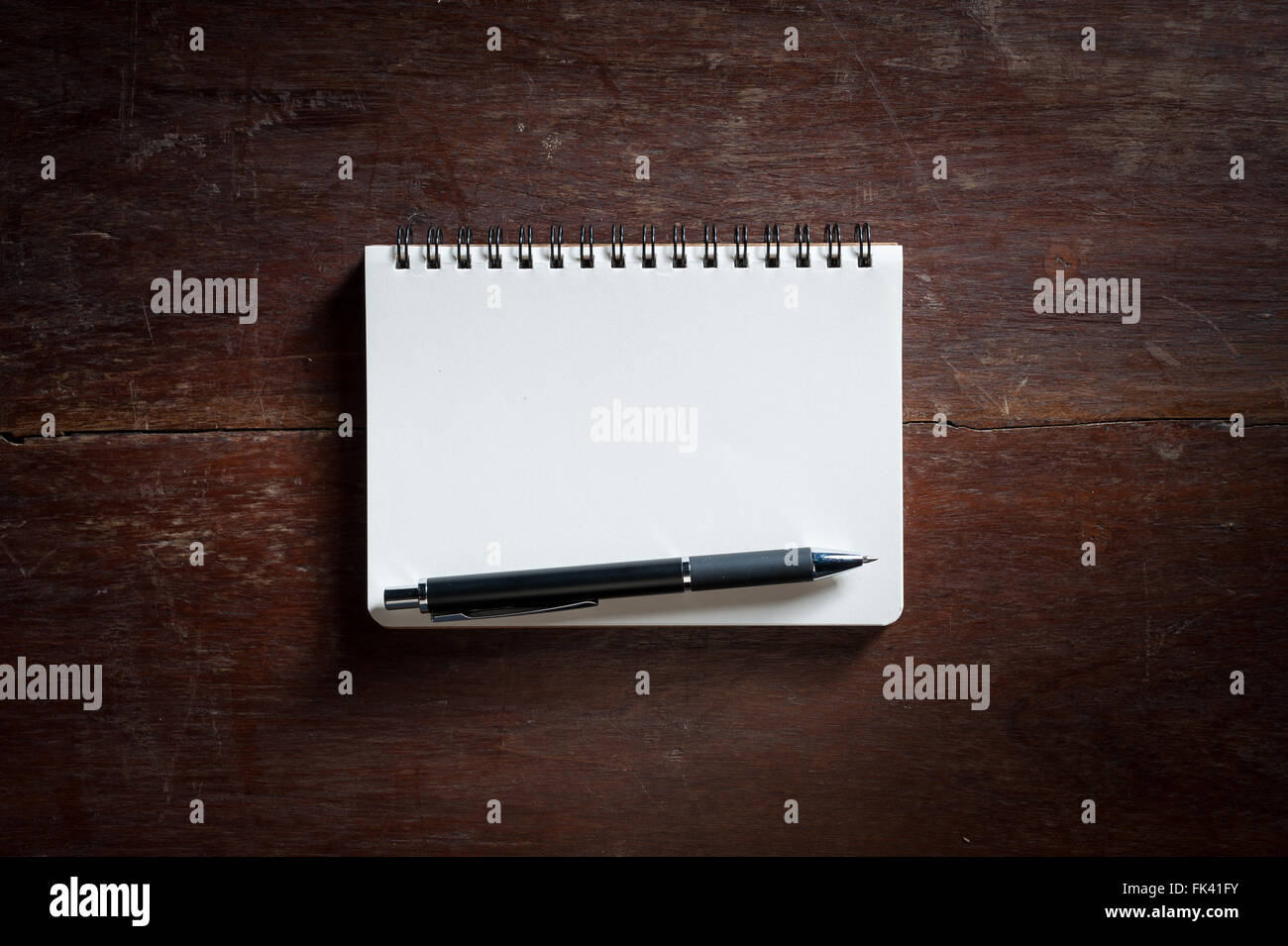 Small opened notepad with blank area for text or message and pen on rustic wood table with low key scene. Stock Photo