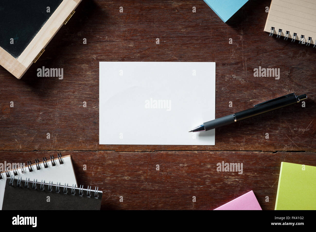 Blank paper with area for text or message, pen, notebook, and sticky paper on wood table with low key scene Stock Photo