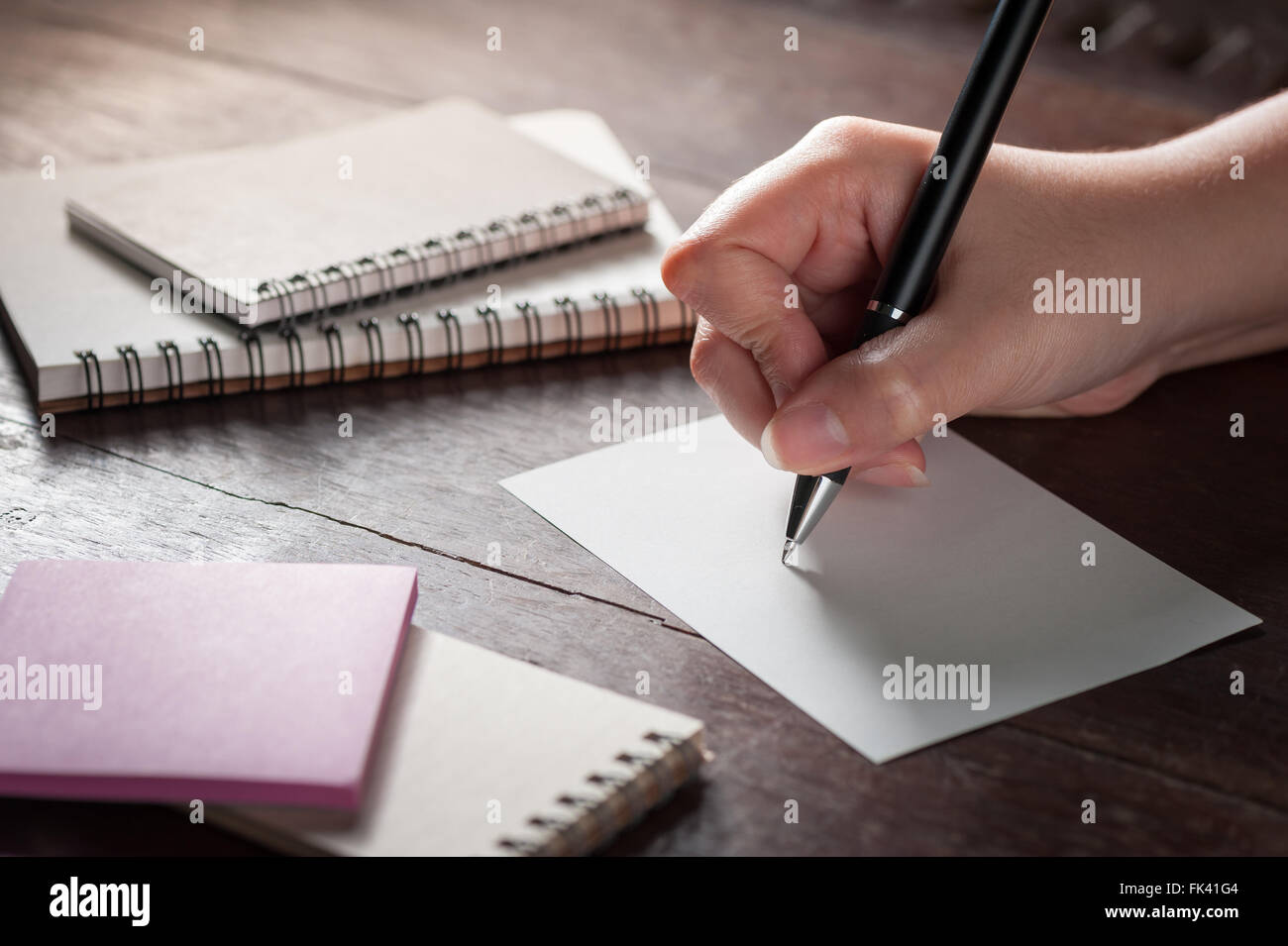 Woman right hand writing on blank paper on wood table with notebooks on wood table with low key scene and vintage filter effect Stock Photo