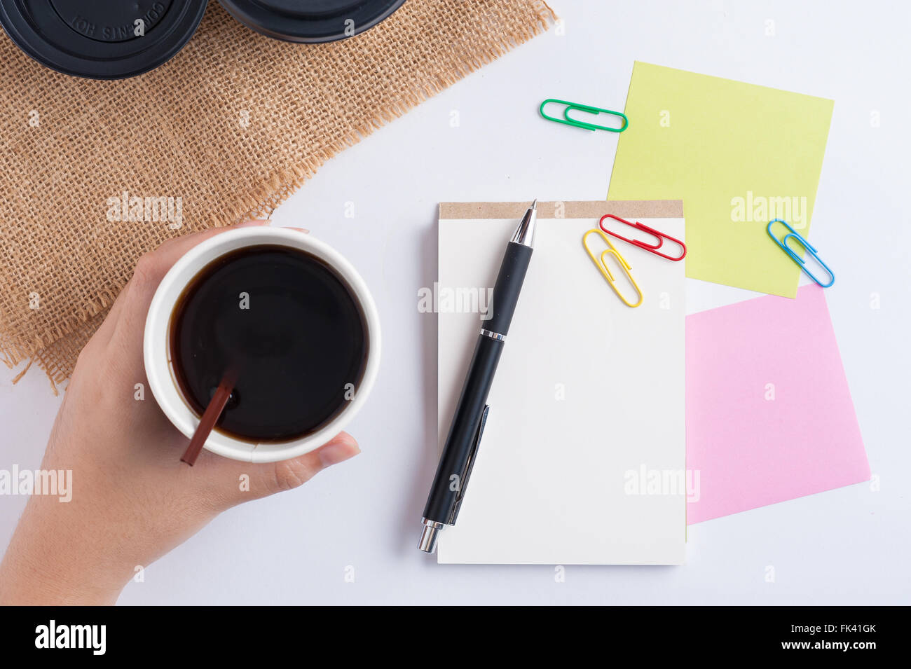 Woman hand holding take away coffee cup beside notepad on office table Stock Photo