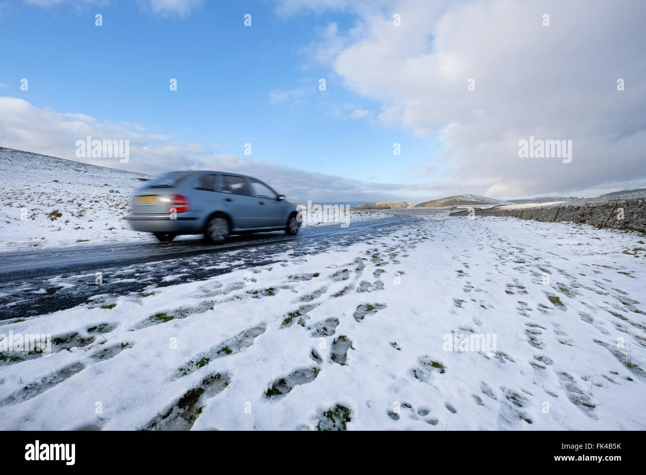 A blurred motion grey estate car being driven over snow covered Malham Moor, North Yorkshire National Park, England UK Stock Photo