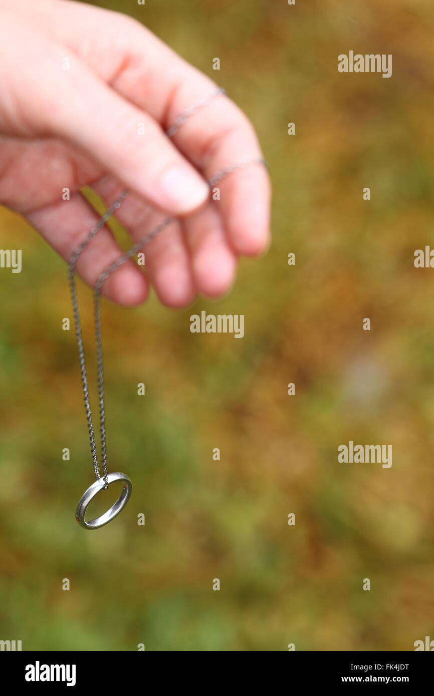 A wedding ring dangling on a chain from a lady's hand. Stock Photo