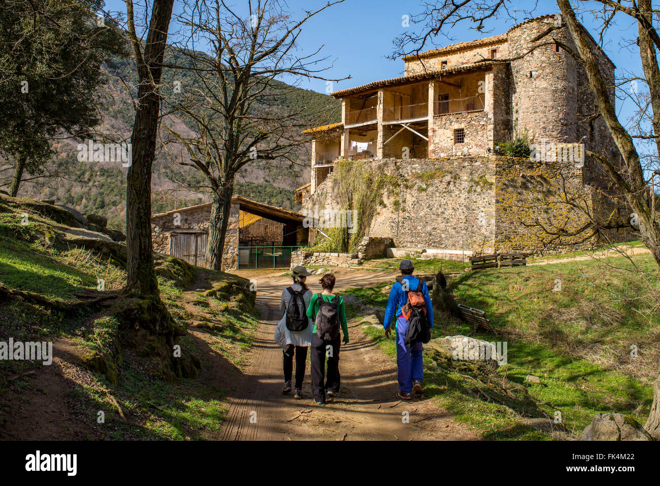 Three hikers walk on a dirt road towards a massive old Spanish farm house. Stock Photo