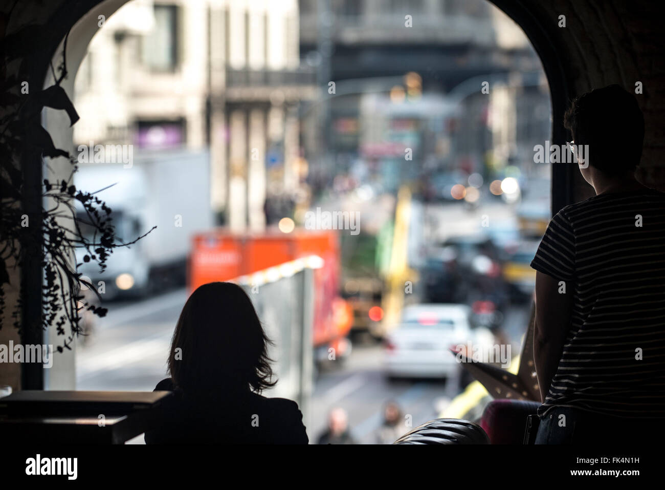 Two women look out an arched window at a city full of traffic. Stock Photo