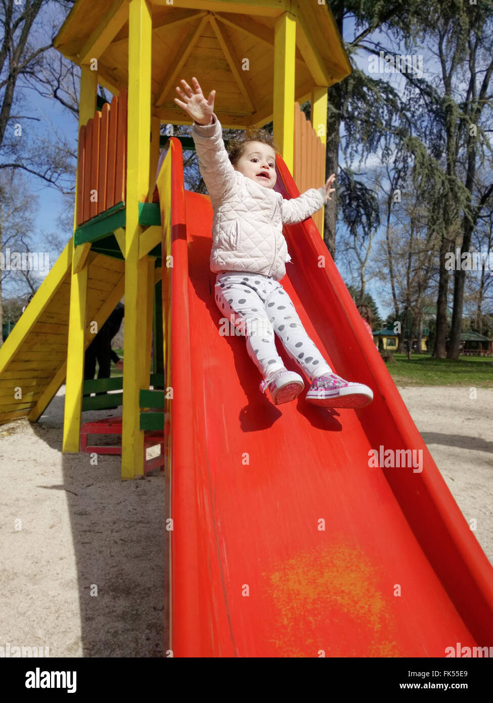 Vertical shot of an excited baby girl sliding down a slide at a