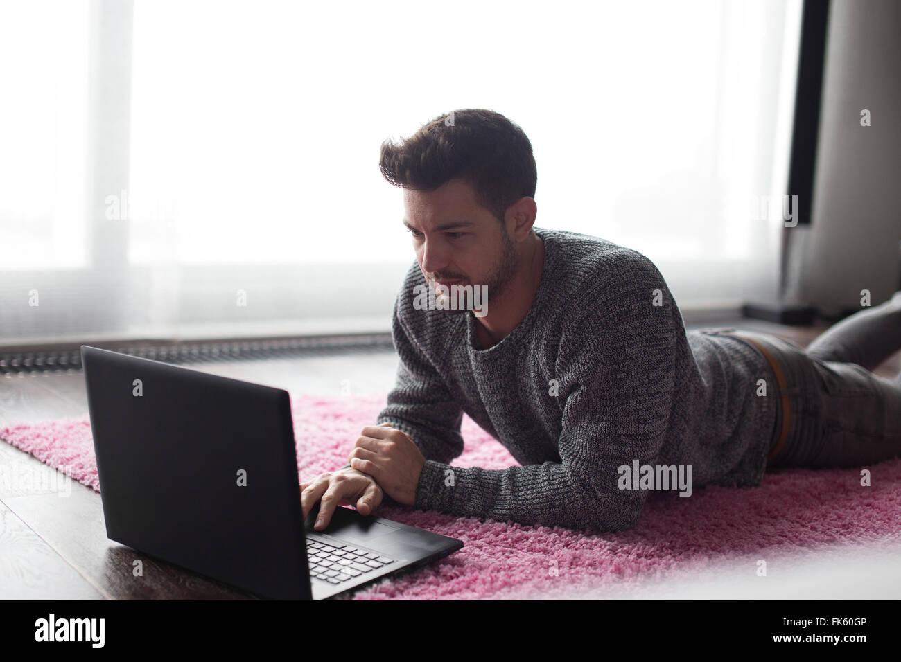 Young man typing on laptop, lie prone on carpet at home Stock Photo