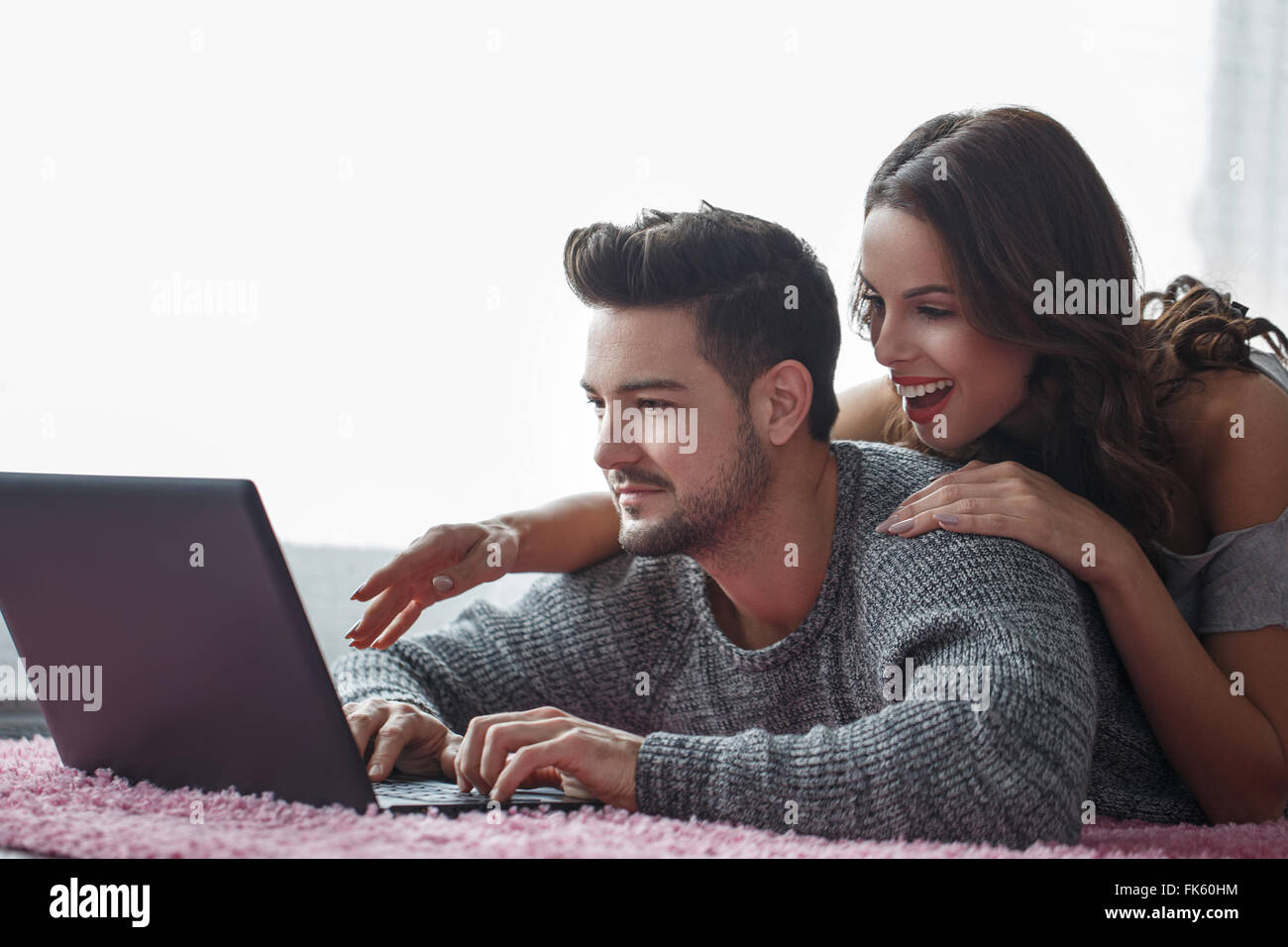 Young couple with laptop lying prone on carpet, wi-fi technology Stock Photo